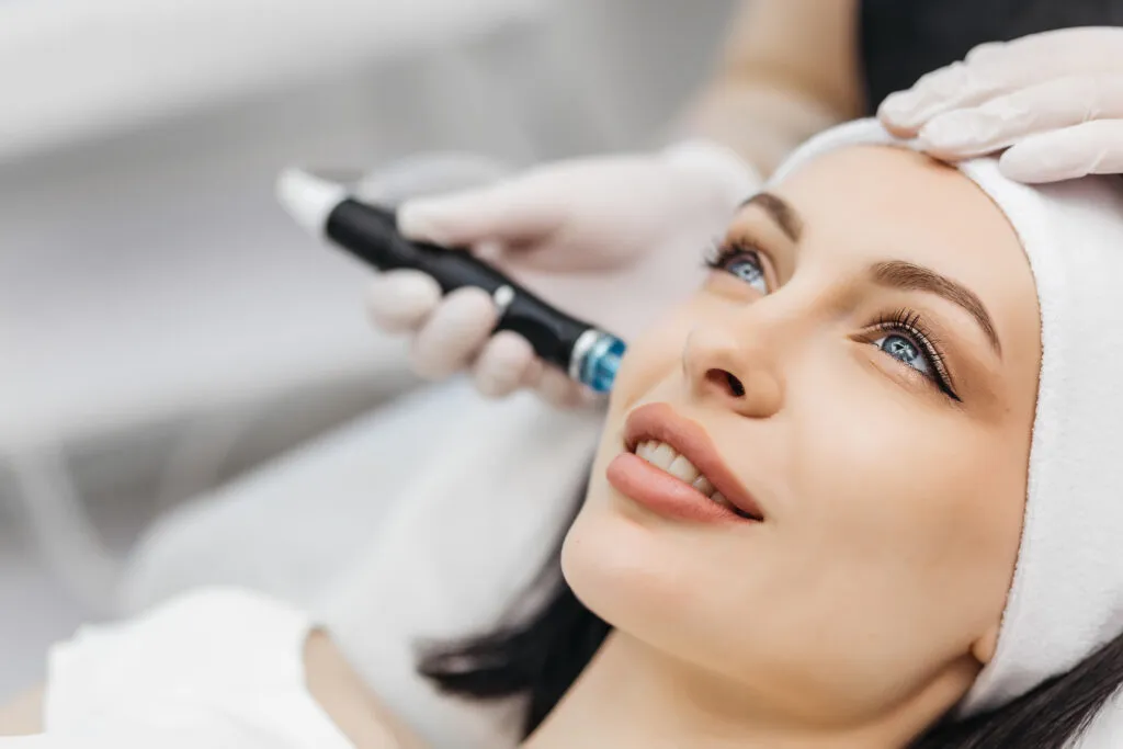 Close-up of a woman receiving a facial treatment with a skincare device from an esthetician wearing gloves